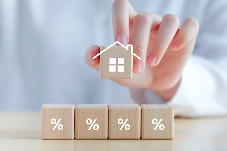 Hand placing a wooden block with a house symbol on top of four blocks marked with percentage signs