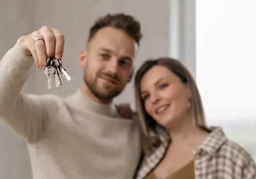 Smiling man holding up a bunch of house keys towards the camera with a woman standing beside him