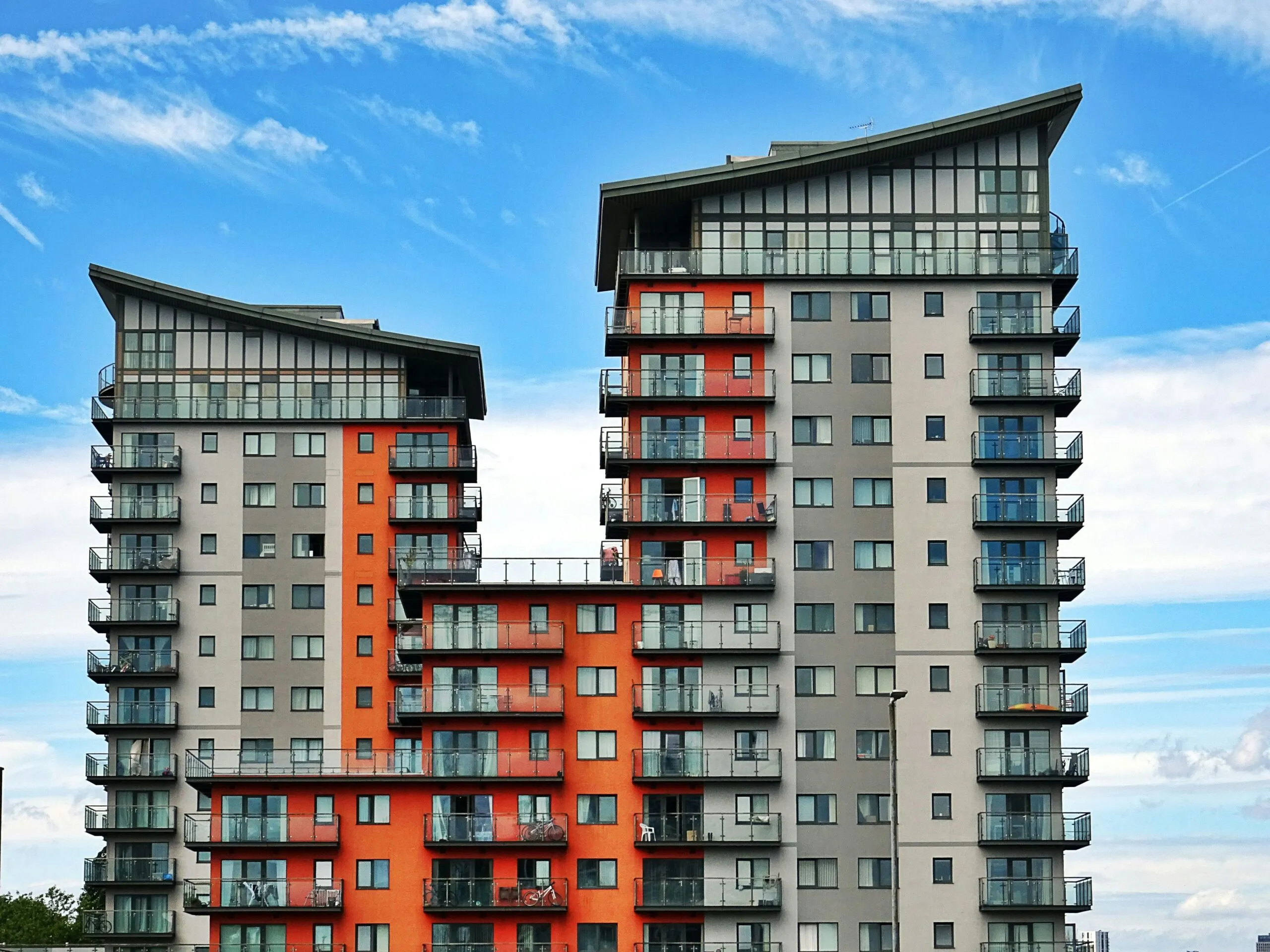 Two modern apartment towers with orange and grey cladding and glass balconies against a blue sky